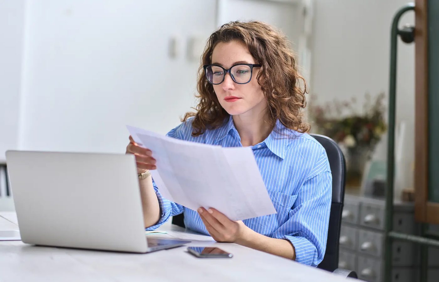 A woman at a laptop reviewing printed documents