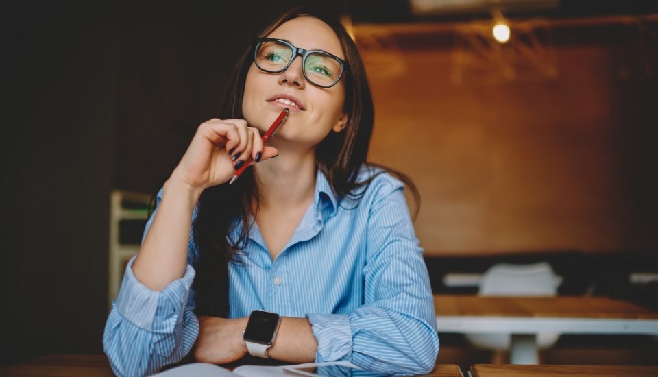 A young woman in glasses smiling as she thinks about her next step